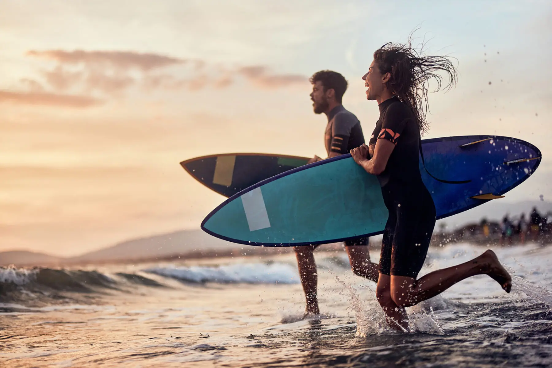 Carefree surfers rushing into sea at sunset. Focus is on woman. Copy space.